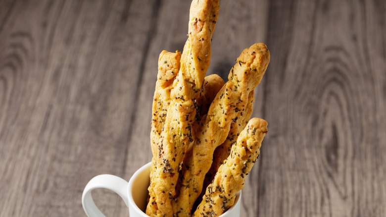 A mug with cheese straws against a grainy, wooden background
