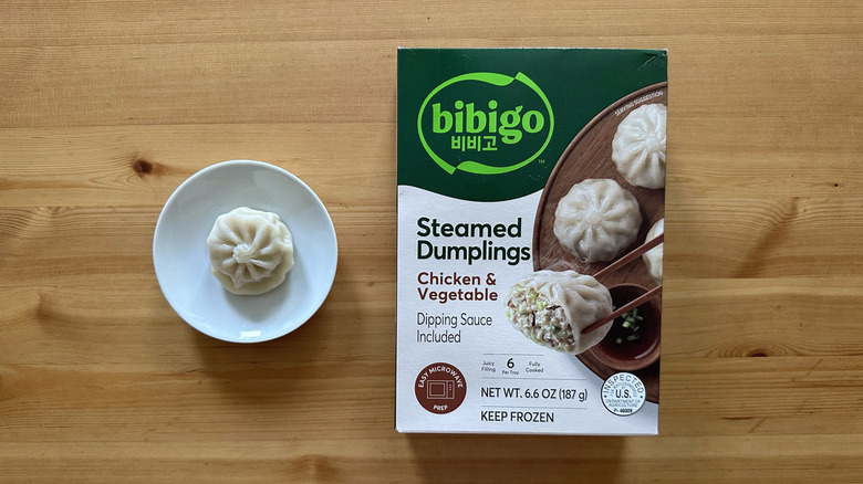 Bibigo Chicken and Vegetable Steamed Dumplings on wooden table with one dumpling on the side
