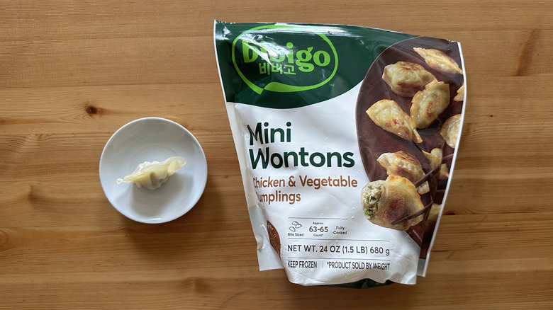 Bibigo Mini Wontons Chicken and Vegetable Dumplings on wooden table with one dumpling on a small plate