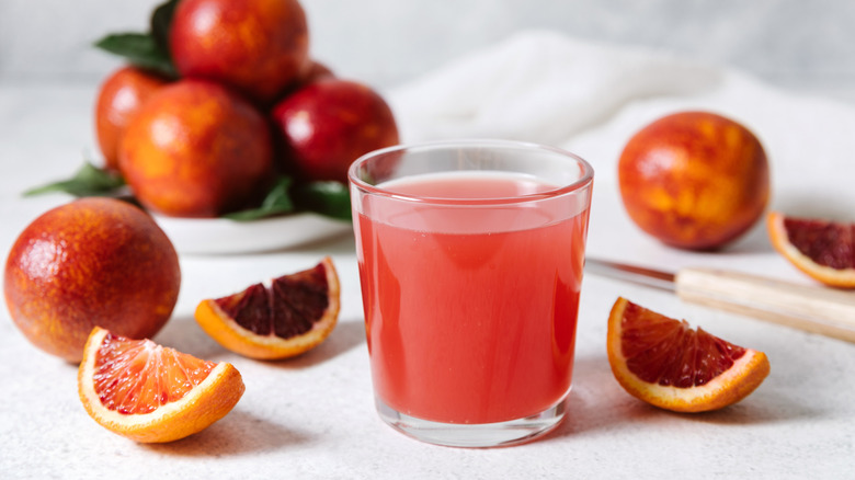 glass of blood orange juice and sliced blood oranges on the side