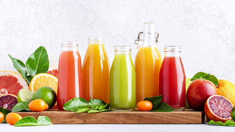 bottles of different fruit juices and fresh fruit on a wooden cutting board and counter