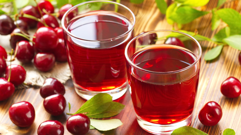 two glasses of cherry juice and cherries on a wooden counter