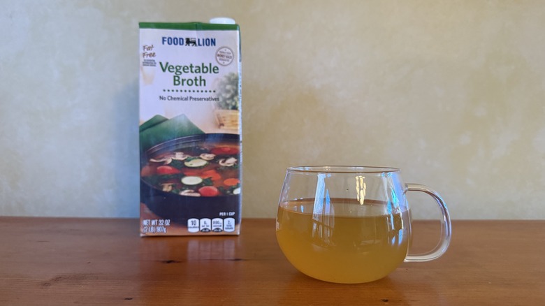 Carton of Food Lion vegetable broth on wooden table with glass of broth