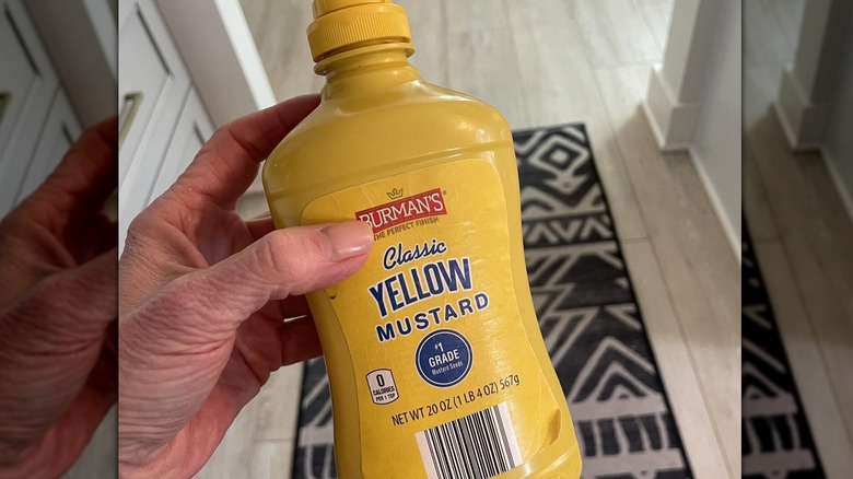 Someone holding up a bottle of Burman's Yellow Mustard.