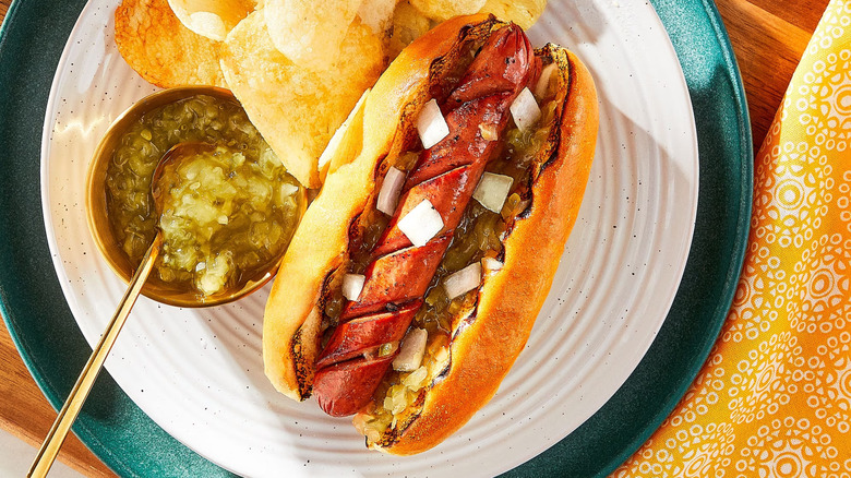 Cup of Great Value Dill Squeeze Relish sitting next to a hot dog and chips on a plate.