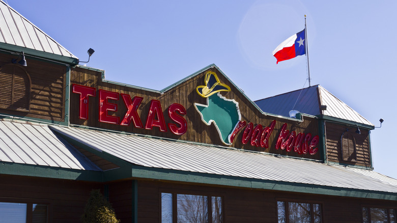 Texas Roadhouse sign on building against blue sky with Texas flag