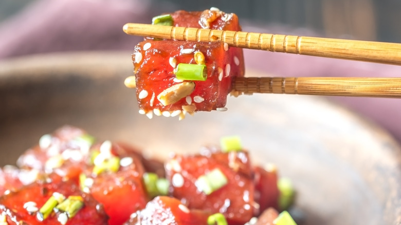 Chopsticks holding a cube of marinated ahi tuna for poke.