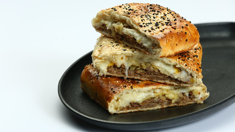 Stacked, sliced stromboli with ground meat and cheese on a black plate