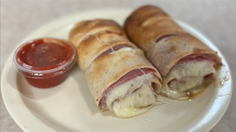 A n overstuffed stromboli from a pizzeria on a white plate with a plastic cup of red sauce