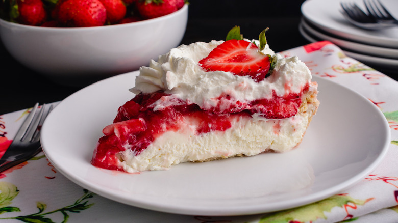 Slice of strawberry cream pie topped with whipped cream and strawberry slice on white plate