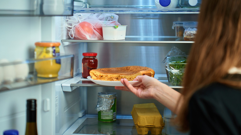 Woman putting pie on plate in fridge
