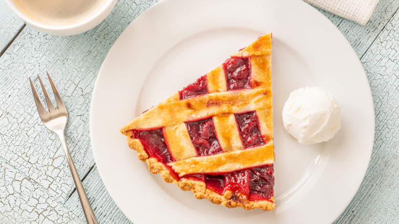 Top-down shot of cherry pie next to scoop of ice cream on white plate