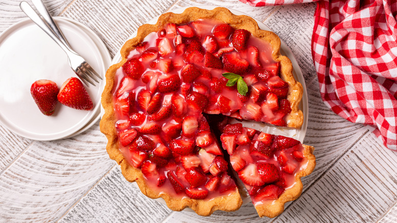 Top-down view of strawberry pie next to plate with strawberries and forks