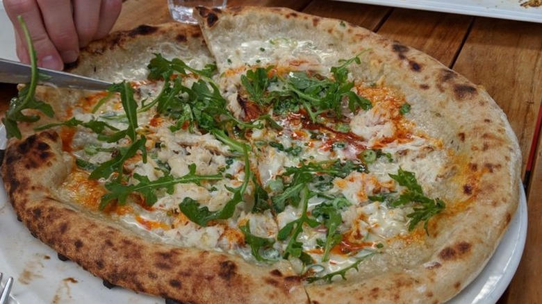 Hand using knife to slice pizza topped with crab and crème fraîche