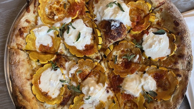 Pizza topped with delicata squash, oregano, and burrata