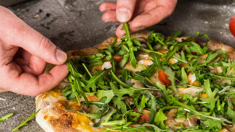 Chef's hands placing arugula leaves on freshly baked pizza