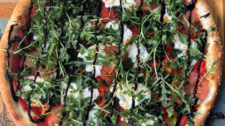 Pizza topped with red sauce, tomato, mozzarella, spinach, arugula, and balsamic drizzle