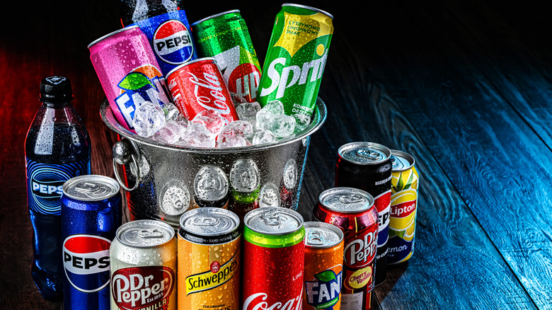 Several cans of soda in and around ice bucket on blue surface