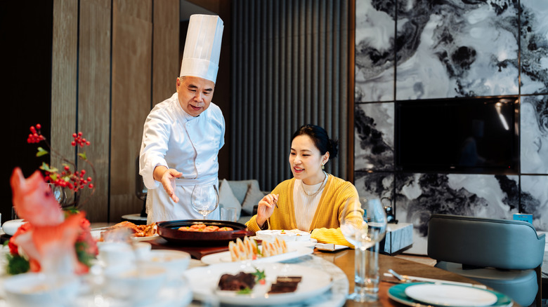Chef gesturing to food in front of smiling customer