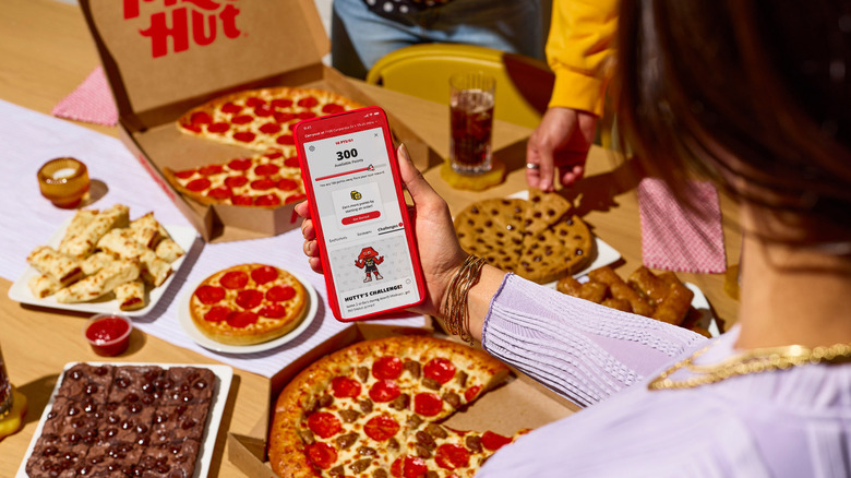 Woman surrounded by Pizza Hut food checking her Pizza Hut rewards on her phone