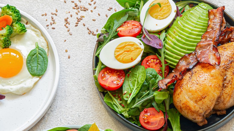 close up of dish with salad, eggs, avocado, bacon and quail, next to white dish with egg and broccoli