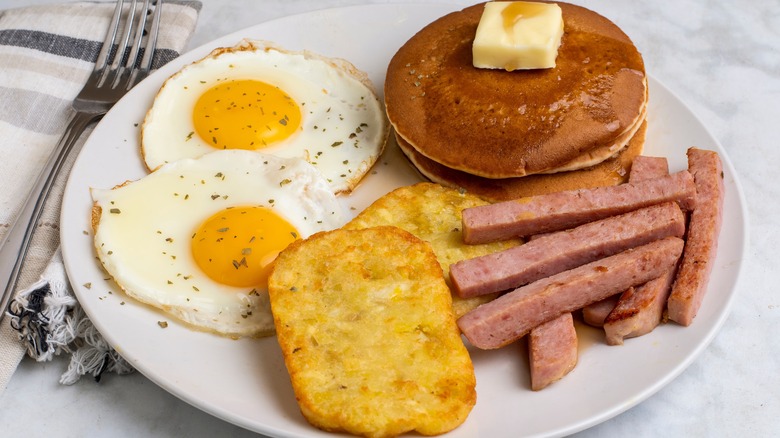 fried eggs top with parsley served with spam fries and pancakes on a white plate