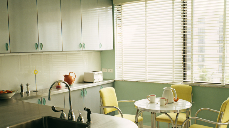 image of a retro pastel green kitchen with a round table and three yellow chairs