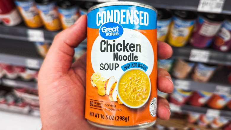 Hand holding can of Great Value chicken noodle soup in Walmart aisle