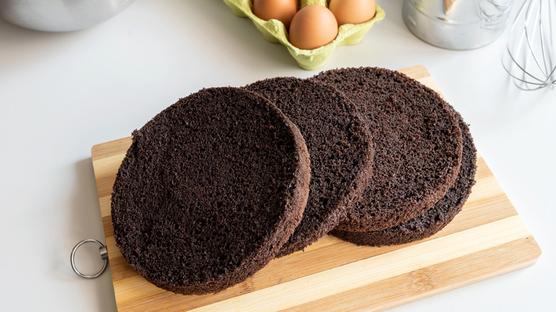 Four round layers of chocolate cake on wooden cutting board