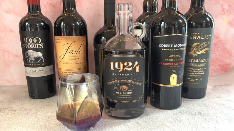 Glass of red wine next to several bottles of bourbon barrel aged red wine on table