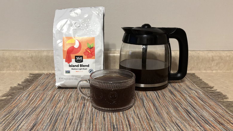 365 Whole Foods Island Blend coffee in bag, brewed in pot, and in glass mug on neutral countertop