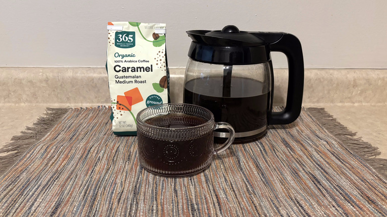 365 Whole Foods Organic Caramel Guatemalan coffee in bag, brewed in pot, and in glass mug on neutral countertop