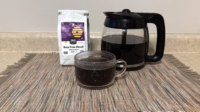 365 Whole Foods Buzz Free Decaf coffee in bag, brewed in pot, and in glass mug on neutral countertop