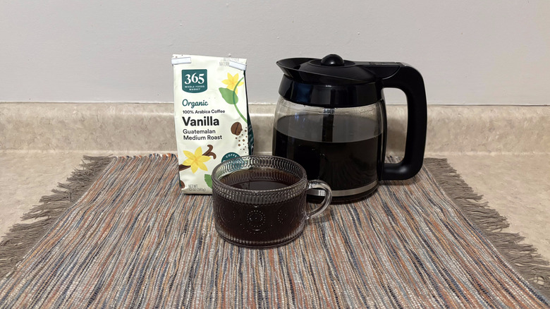 365 Whole Foods Organic Vanilla Guatemalan coffee in bag, brewed in pot, and in glass mug on neutral countertop
