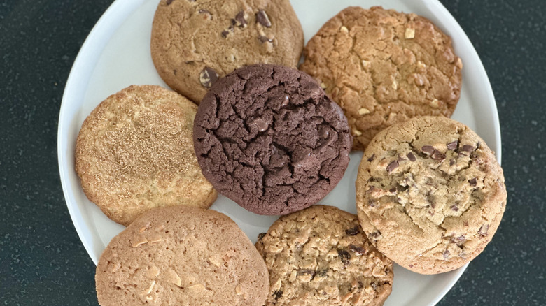 Overhead image of white plate on black counter with seven different cookies