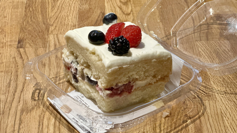 Plastic container of slice of Whole Foods Berry Chantilly Cake on wooden countertop