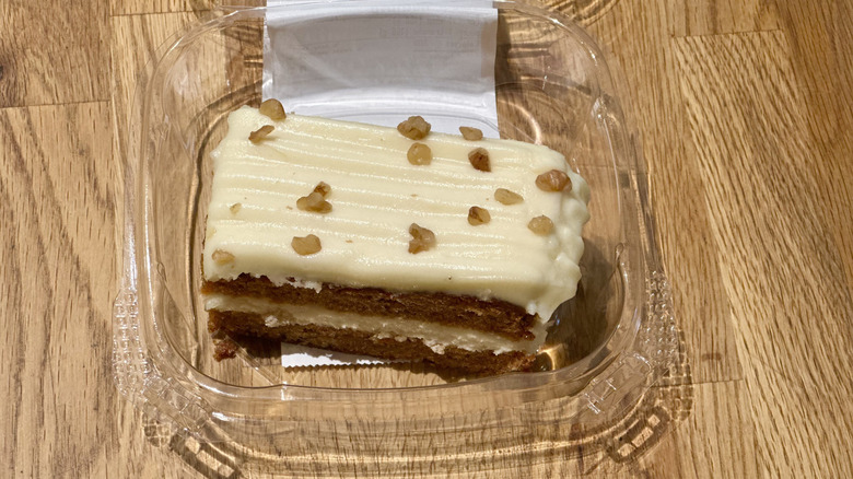 Plastic container of slice of Whole Foods Carrot Cake on wooden countertop