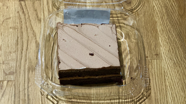 Plastic container of slice of Whole Foods Chocolate Cake on wooden countertop