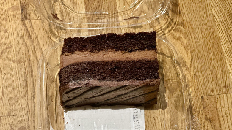 Plastic container of slice of Whole Foods Chocolate Eruption Cake on wooden countertop