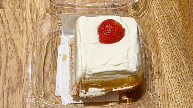 Plastic container of slice of Whole Foods Strawberry Shortcake on wooden countertop