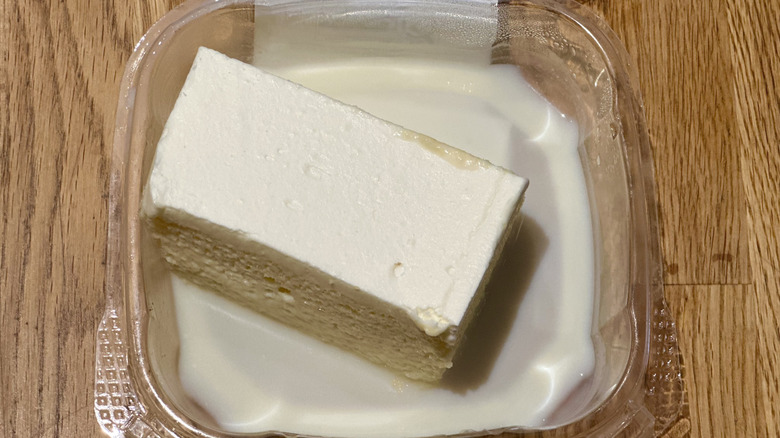 Plastic container of slice of Whole Foods Tres Leches Cake on wooden countertop
