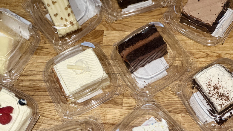 Angled shot of multiple plastic containers of cake slices from Whole Foods on wooden counter