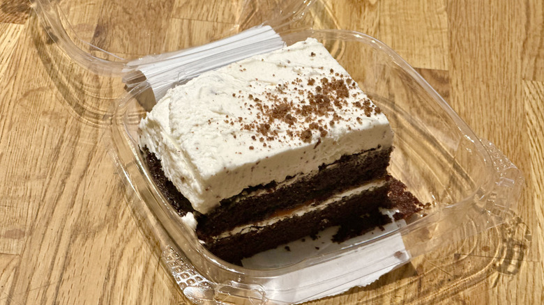 Plastic container of slice of Whole Foods Brown Butter Cookie Caramel Crunch Cake on wooden countertop