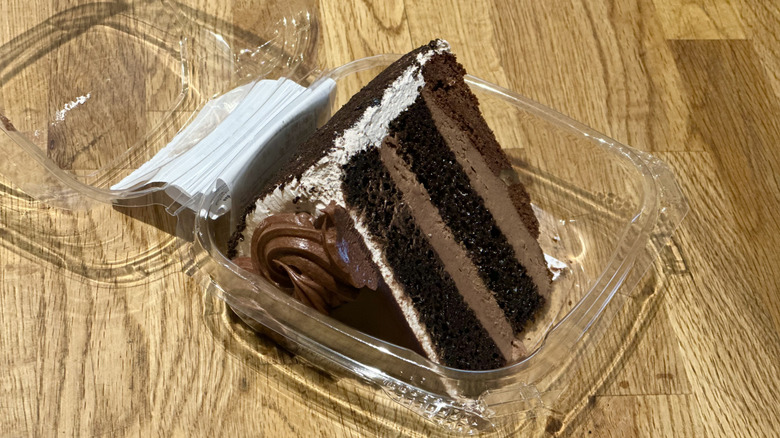 Plastic container of slice of Whole Foods Death by Chocolate Cake on wooden countertop