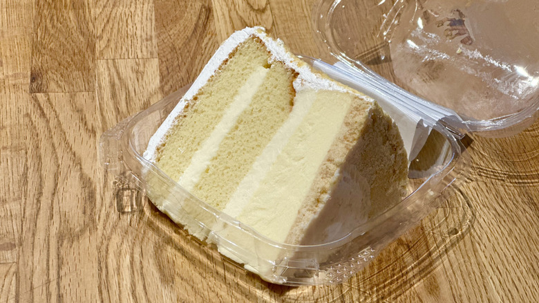 Plastic container of slice of Whole Foods Triple Vanilla Bean Cake on wooden countertop