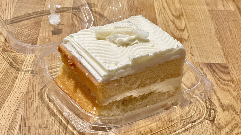 Plastic container of slice of Whole Foods Vanilla Cake on wooden countertop