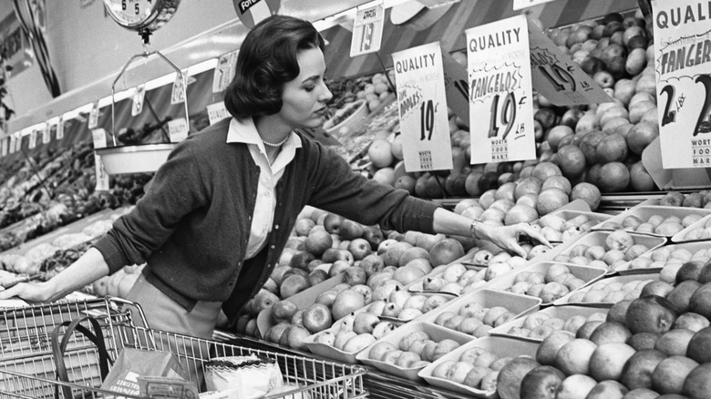 Woman selecting produce and pushing a cart in an old-fashioned grocery store