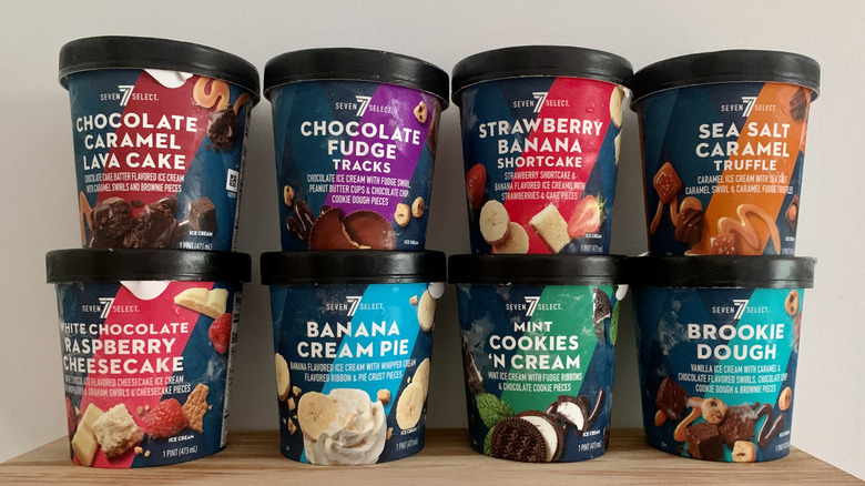 eight unopened pints of 7-Select ice cream stacked on wood shelf with white backgound