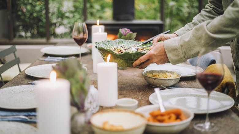 wood table with plates on it and bowls with food in them, wine and candles on table