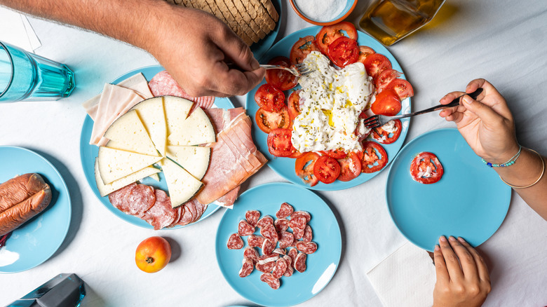 blue plates with cheese, tomato slices; people reaching for food on blue plates